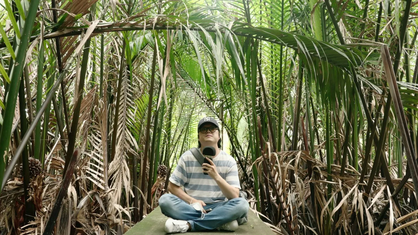 밀림 한가운데 홀로 앉아 마이크를 들고 위를 올려다보는 모습
