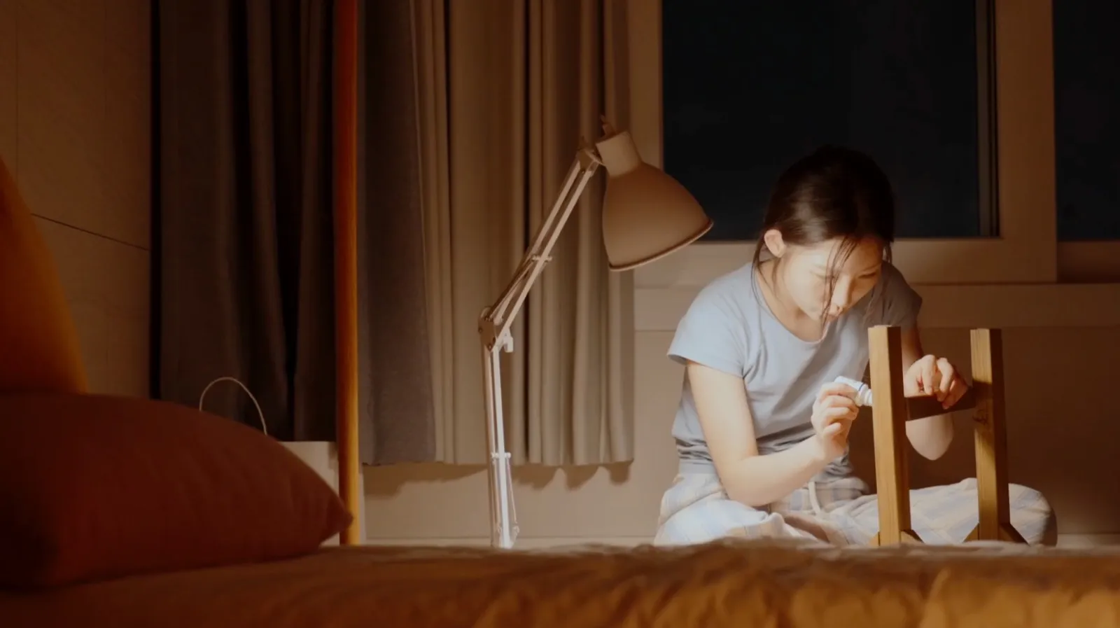 At night, under a single lamp, tightening a chair leg on the bed